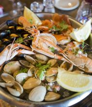 Heerlijk eten bij de echt Ierse Crabby Jo's in Dublin. De zeevruchtenschotel met garnalen, mosselen, venusschelpen en versierd met partjes citroen en verse kruiden. Het wordt geserveerd in een metalen schaal op een houten tafel met wijnglazen en geruite servetten op de achtergrond.