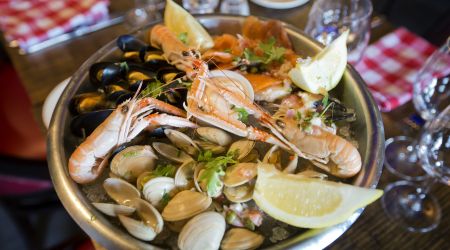 Heerlijk eten bij de echt Ierse Crabby Jo's in Dublin. De zeevruchtenschotel met garnalen, mosselen, venusschelpen en versierd met partjes citroen en verse kruiden. Het wordt geserveerd in een metalen schaal op een houten tafel met wijnglazen en geruite servetten op de achtergrond.
