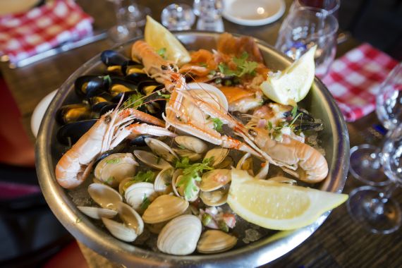Heerlijk eten bij de echt Ierse Crabby Jo's in Dublin. De zeevruchtenschotel met garnalen, mosselen, venusschelpen en versierd met partjes citroen en verse kruiden. Het wordt geserveerd in een metalen schaal op een houten tafel met wijnglazen en geruite servetten op de achtergrond.