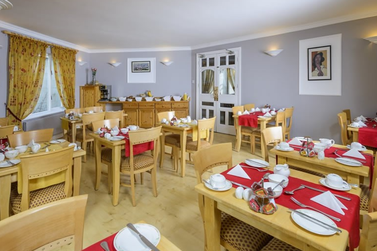Een lichte eetkamer in Fanad House, een charmant bed and breakfast in Kilkenny, heeft lichte houten tafels gedekt voor het ontbijt met rode lopers, witte borden en gevouwen servetten. Gele bloemetjesgordijnen omlijsten de ramen; kunstwerken versieren de grijze muren. | Echt Ierland Vakanties