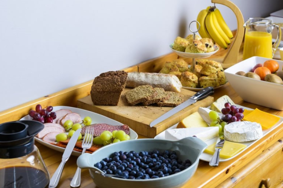 Een charmant ontbijt in een pension in Kilkenny bestaat uit gesneden brood, kaas, ham, druiven, bosbessen, scones, bananen op een standaard, sinaasappels, kiwi's, sinaasappelsap in een kan en een koffiepot - allemaal prachtig verzorgd in Fanad House. | Echt Ierland Vakanties