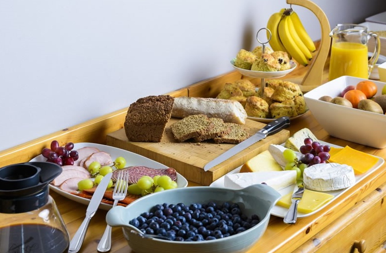 Een charmant ontbijt in een pension in Kilkenny bestaat uit gesneden brood, kaas, ham, druiven, bosbessen, scones, bananen op een standaard, sinaasappels, kiwi's, sinaasappelsap in een kan en een koffiepot - allemaal prachtig verzorgd in Fanad House. | Echt Ierland Vakanties