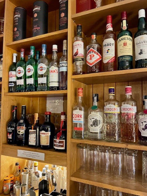 In Boetiek hotel Westport staan flessen gin, whiskey en likeuren netjes op houten planken. Onder de flessen staat leeg glaswerk ondersteboven naast benodigdheden om cocktails te maken en servetten op een lagere toonbank. | Echt Ierland Vakanties