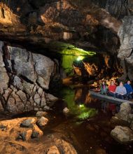 De reizigers ontdekken een van de grotten van Ierland. Zachte lichten verlichten de grot, werpen reflecties op stilstaand water en benadrukken groene en bruine tinten in dit ondergrondse wonderen Ierland. | Echt Ierland Vakanties