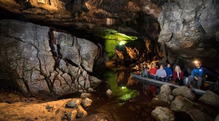 De reizigers ontdekken een van de grotten van Ierland. Zachte lichten verlichten de grot, werpen reflecties op stilstaand water en benadrukken groene en bruine tinten in dit ondergrondse wonderen Ierland. | Echt Ierland Vakanties