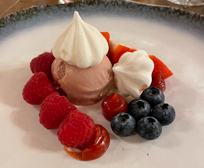 Op een dessertbord in Boetiek hotel Westport staat een bolletje roze roomijs met daarop witte meringue koekjes, omringd door verse frambozen, bosbessen, plakjes aardbeien en rode saus op een wit en blauw gradiënt bord. | Echt Ierland Vakanties