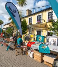 Buitenmarkt op een zonnige dag in Howth, vlakbij Dublin, met tafels met kleurrijke kunstreproducties en t-shirts. Ontdek met ons dit kleurrijke vissersdorp | Echt Ierland Vakanties