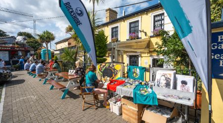 Buitenmarkt op een zonnige dag in Howth, vlakbij Dublin, met tafels met kleurrijke kunstreproducties en t-shirts. Ontdek met ons dit kleurrijke vissersdorp | Echt Ierland Vakanties