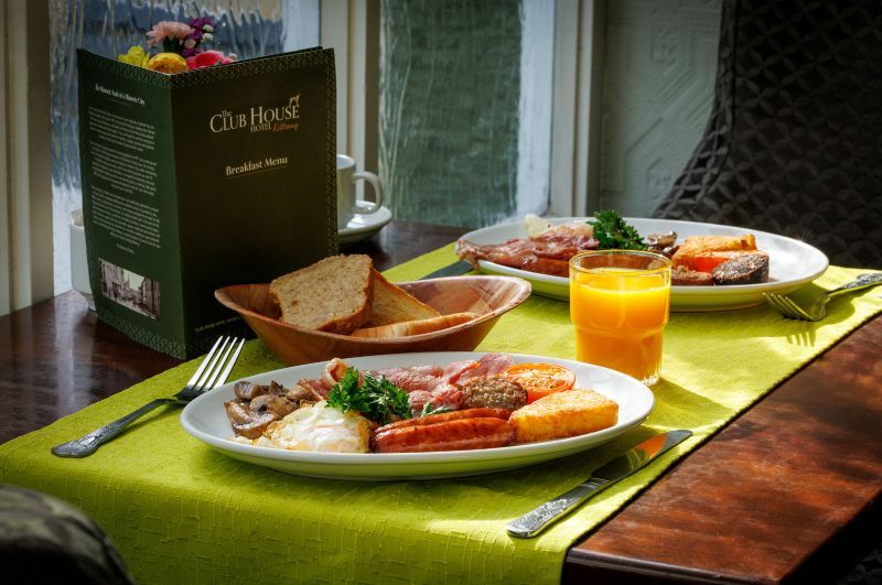 Twee borden met een volledig Engels ontbijt liggen op een groene placemat in een charmant boetiekhotel in het centrum van Killarney. Verse jus d'orange, een broodmandje en een ontbijtmenu maken het gezellige tafereel bij het lichte raam compleet. | Echt Ierland Vakanties