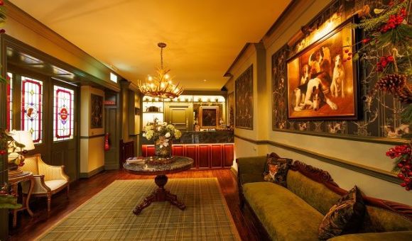 Een warm verlichte lobby in vintage-stijl in een charmant boetiekhotel in het centrum van Killarney heeft een groene fluwelen bank, sierlijke fauteuils, een ronde tafel met bloemen, behang met patronen, een kroonluchter, gebrandschilderde glazen deuren en een schilderij van honden boven de bank. | Echt Ierland Vakanties