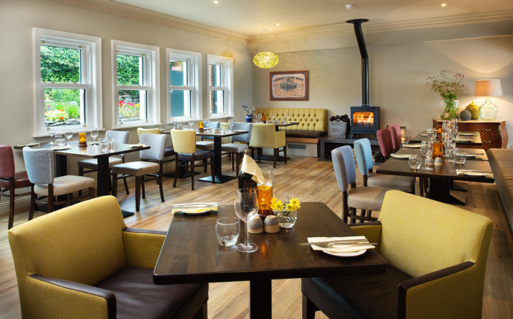 Een gezellige, goed verlichte eetzaal met een moderne inrichting en een vleugje charme van de oude wereld, met houten tafels, stoelen met kussens in neutrale tinten, grote ramen, een houtkachel en verse bloemen - perfect voor een boetiekhotel in het centrum van Kilkenny. | Echt Ierland Vakanties
