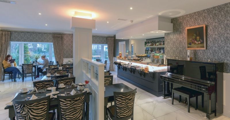 Elegant restaurantinterieur in het Hillyard House Hotel in Castlewellan, met stoelen met zebraprint, zwarte tafels met wit servies, een buffet en een piano. Grote ramen vullen de ruimte met licht; sierlijk behang en kunst sieren de muren. | Echt Ierland Vakanties