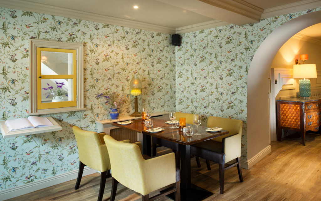 Een gezellige eethoek met ouderwetse charme heeft een donkerhouten tafel voor vier personen, lichtgele gestoffeerde stoelen, behang met bloemmotieven en een decoratieve boog die de uitnodigende sfeer van een boetiekhotel in het centrum van Kilkenny weerspiegelt. | Echt Ierland Vakanties